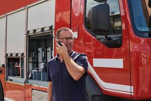 A dedicated firefighter, captured in a moment of communication, stands before a modern firetruck, showcasing the seamless integration of technology in emergency response photo