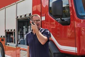 A dedicated firefighter, captured in a moment of communication, stands before a modern firetruck, showcasing the seamless integration of technology in emergency response photo