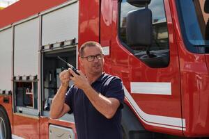 A dedicated firefighter, captured in a moment of communication, stands before a modern firetruck, showcasing the seamless integration of technology in emergency response photo