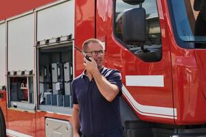 A dedicated firefighter, captured in a moment of communication, stands before a modern firetruck, showcasing the seamless integration of technology in emergency response photo