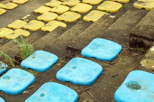 Old, blue plastic stadium seats with bright yellow seats in the background going up a level with weeds growing through the cracks between each row of seats. Abandoned Waterpark, Hue, Vietnam. photo