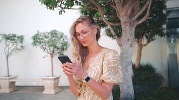 Happy woman using smartphone by tree on footpath video