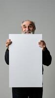 A mature man with a beard holds up a blank white sign photo
