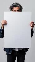 A mature man holding a blank white sign in front of his face, expressing sadness photo