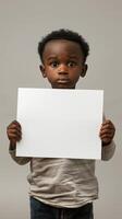 A young boy with a black afro holds up a blank white sign with a somber expression photo