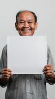 A mature man in Thailand smiles while holding up a blank white sheet of paper photo