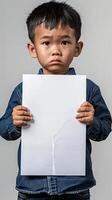 A Chinese sad little boy holding up a blank white piece of paper photo