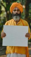 A man in a colorful turban holds a blank sign photo
