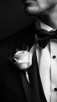 A man in a tuxedo, featuring a groom boutonniere, exudes sophistication in black and white photo