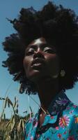 Black and white photo of a woman with an afro looking up, standing in a field of wheat