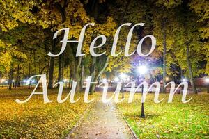 The words Hello Autumn on the background of night city park with fallen leaves and trees. Greeting card. The concept of the beginning of autumn. photo