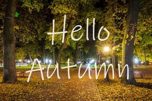 The words Hello Autumn on the background of night city park with fallen leaves and trees. Greeting card. The concept of the beginning of autumn. photo