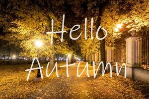 The words Hello Autumn on the background of night city park with fallen leaves and trees. Greeting card. The concept of the beginning of autumn. photo