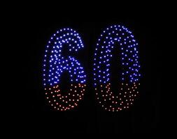 Drone light shows on black night sky background. A figure of the number sixty, six, zerro, 60 made of glowing drones. photo