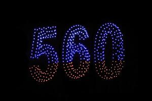 Drone light shows on black night sky background. A figure of the number five hundred and sixty, six, five, zerro, 560 made of glowing drones. photo
