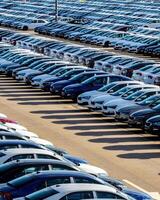 Rows of a new cars parked in a distribution center on a car factory on a sunny day. photo