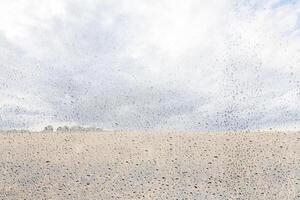 Agricultural field after rain with clouds in the sky behind wet glass in golden autumn. Bad weather concept. Abstract landscape. photo