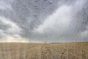 Agricultural field after rain with clouds in the sky behind wet glass in golden autumn. Bad weather concept. Abstract landscape. photo