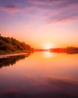 Sunset or dawn on a river with a cloudy sky and sun rays reflected in the water, water lilies and trees growing along the shore. photo