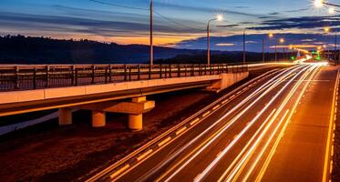 Traces of headlights from cars moving at night on the bridge, illuminated by lanterns. Abstract cityscape with highway at dusk. photo