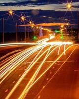 Traces of headlights from cars moving at night on the bridge, illuminated by lanterns. Abstract cityscape with highway at dusk. photo