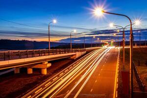 Traces of headlights from cars moving at night on the bridge, illuminated by lanterns. Abstract cityscape with highway at dusk. photo