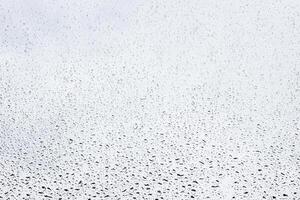 Rain drops on window glasses surface with gray sky background . Natural backdrop of raindrops. Abstract overlay for design. The concept of rainy weather. photo