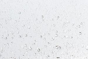 Rain drops on window glasses surface with gray sky background . Natural backdrop of raindrops. Abstract overlay for design. The concept of rainy weather. photo