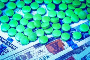 Green pills on the background of one hundred dollar bills. The concept of the expensive cost of healthcare or financing medicine. photo