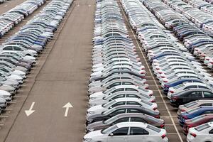 Rows of a new cars parked in a distribution center on a car factory on a cloudy day. Top view to the parking in the open air. photo