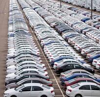Rows of a new cars parked in a distribution center on a car factory on a cloudy day. Top view to the parking in the open air. photo