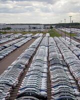Rows of a new cars parked in a distribution center on a cloudy day in the spring, a car factory. Top view to the parking in the open air. photo