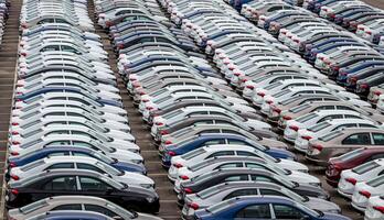 Rows of a new cars parked in a distribution center on a car factory on a cloudy day. Top view to the parking in the open air. photo
