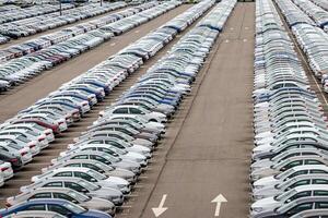 Rows of a new cars parked in a distribution center on a cloudy day in the spring, a car factory. Top view to the parking in the open air. photo