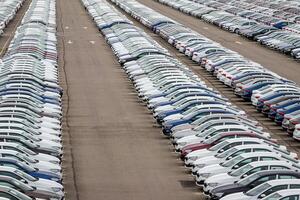 Rows of a new cars parked in a distribution center on a cloudy day in the spring, a car factory. Top view to the parking in the open air. photo