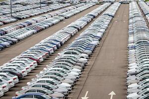 Rows of a new cars parked in a distribution center on a car factory on a cloudy day. Top view to the parking in the open air. photo