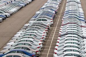Rows of a new cars parked in a distribution center on a cloudy day in the spring, a car factory. Top view to the parking in the open air. photo