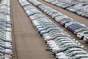 Rows of a new cars parked in a distribution center on a car factory on a cloudy day. Top view to the parking in the open air. photo