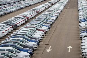 Rows of a new cars parked in a distribution center on a cloudy day in the spring, a car factory. Top view to the parking in the open air. photo