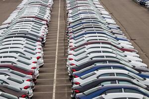 Rows of a new cars parked in a distribution center on a cloudy day in the spring, a car factory. Top view to the parking in the open air. photo