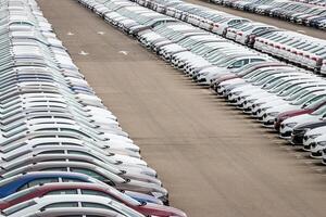 Rows of a new cars parked in a distribution center on a cloudy day in the spring, a car factory. Top view to the parking in the open air. photo
