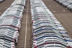 Rows of a new cars parked in a distribution center on a car factory on a cloudy day. Top view to the parking in the open air. photo