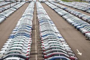 Rows of a new cars parked in a distribution center on a car factory on a cloudy day. Top view to the parking in the open air. photo