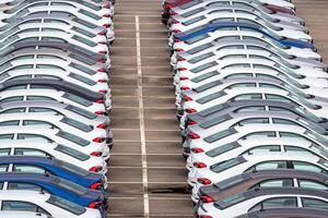 Rows of a new cars parked in a distribution center on a car factory on a cloudy day. Top view to the parking in the open air. photo