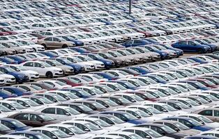 Rows of a new cars parked in a distribution center on a cloudy day in the spring, a car factory. Top view to the parking in the open air. photo