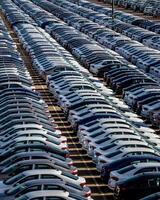 Rows of a new cars parked in a distribution center on a car factory on a sunny day. Top view to the parking in the open air. photo