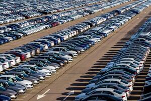 Rows of a new cars parked in a distribution center on a car factory on a sunny day. Top view to the parking in the open air. photo