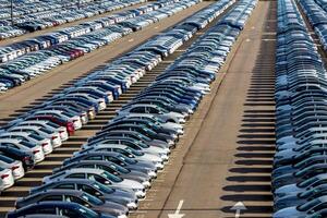Rows of a new cars parked in a distribution center on a car factory on a sunny day. Top view to the parking in the open air. photo