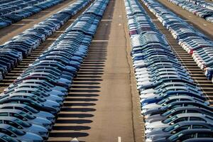 Rows of a new cars parked in a distribution center on a car factory on a sunny day. Parking in the open air. photo