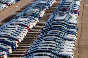 Rows of a new cars parked in a distribution center on a car factory on a sunny day. Top view to the parking in the open air. photo